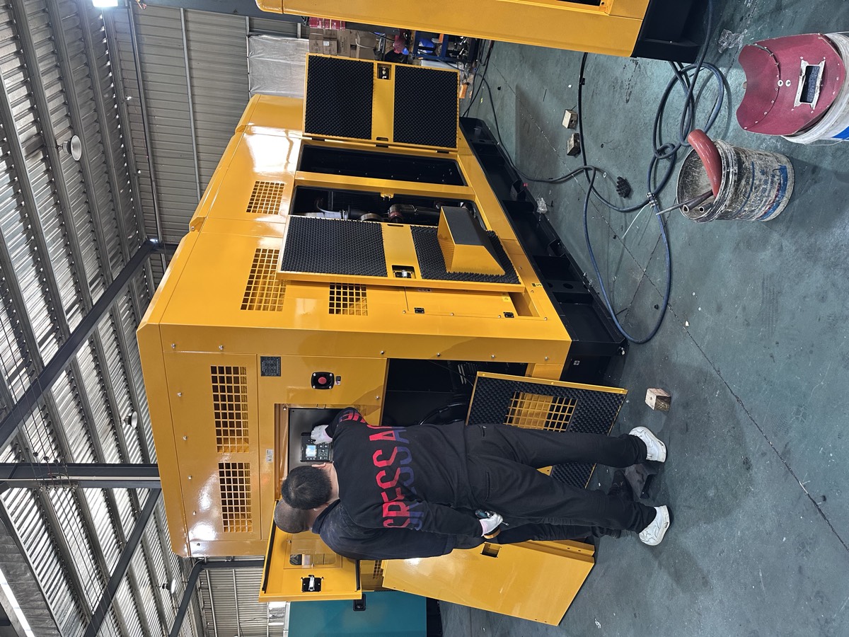 Factory workers inspecting a large yellow silent diesel generator with its service doors open in the production workshop